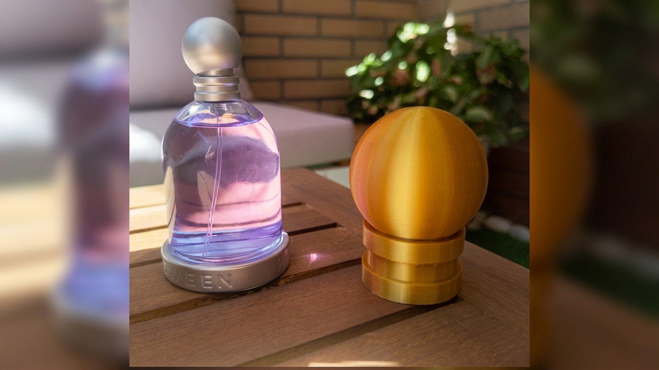 Réplica de tapón de perfume impresa en 3D en PLA silk dorado junto a la botella original - diseño 3D a medida en Getafe